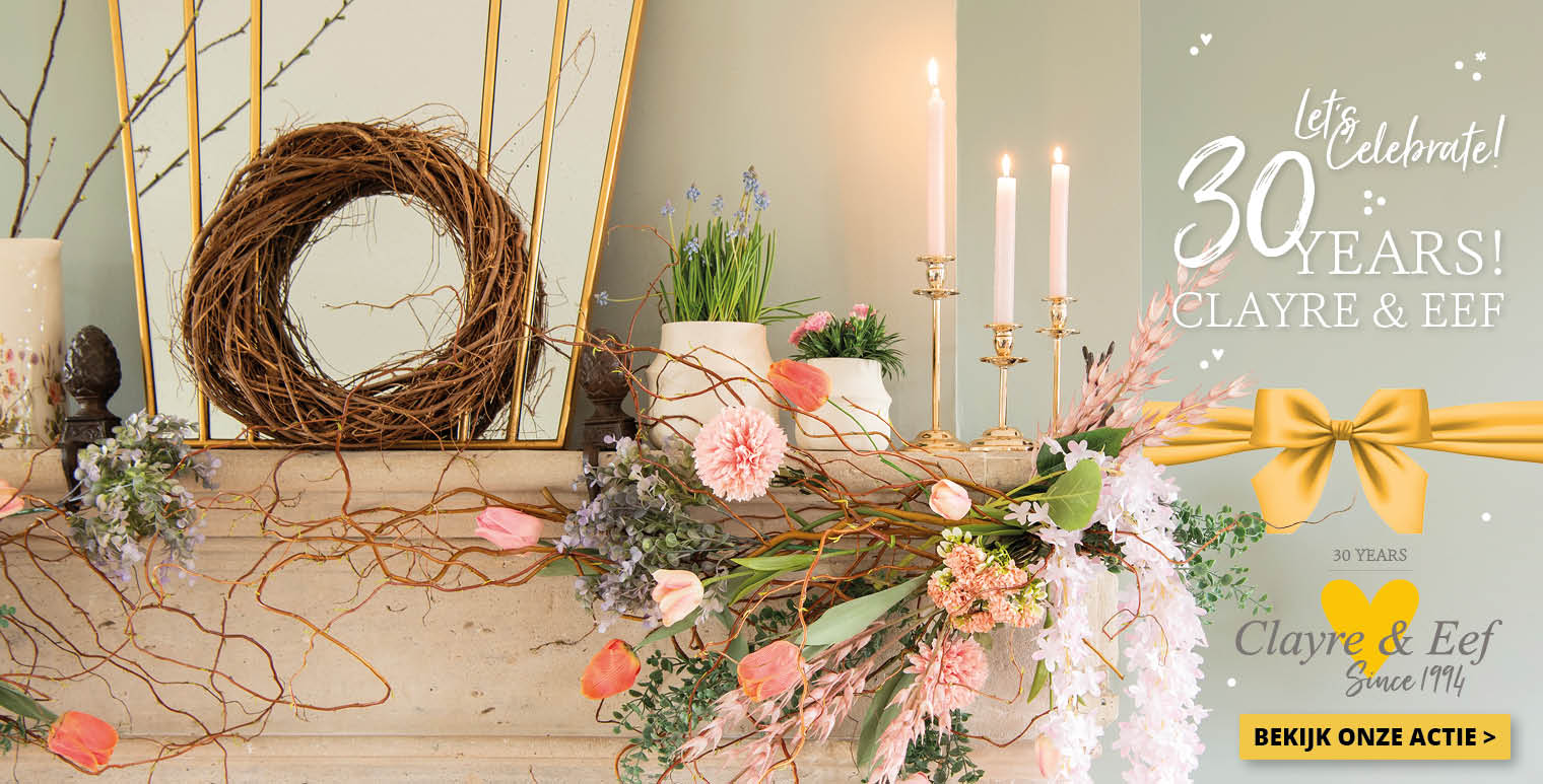 Een feestelijke decoratie die het 30-jarig jubileum viert van Clayre & Eef. Centraal in de compositie is een stijlvolle open haard met daarop een rijke schikking van bloemen en planten, waaronder roze tulpen en zachte bloesems, die samen een lenteachtige sfeer uitstralen. Een natuurlijke, krans van takken hangt tegen de spiegel, toevoegend aan het rustieke en huiselijke thema. Verspreid over de mantel staan elegante kaarsen in gouden kandelaars, die een warme gloed werpen op de omgeving. De scene is versierd met een groot, goudkleurig lint met een strik, en de woorden "Let's Celebrate! 30 Years! CLAYRE & EEF" zijn prominent in sierlijke witte letters aan de bovenkant van de afbeelding weergegeven, wat een uitnodigende en feestelijke sfeer creëert. Het algehele beeld is er een van elegantie en viering, passend voor een speciale mijlpaal.